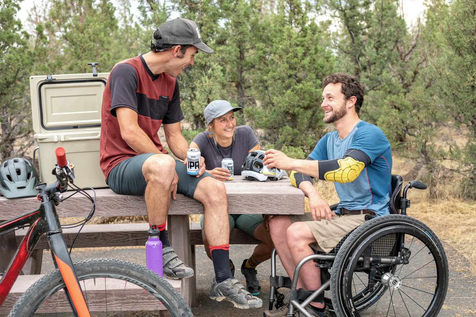 Friends, including a man using a wheelchair, laughing together at an outdoor table