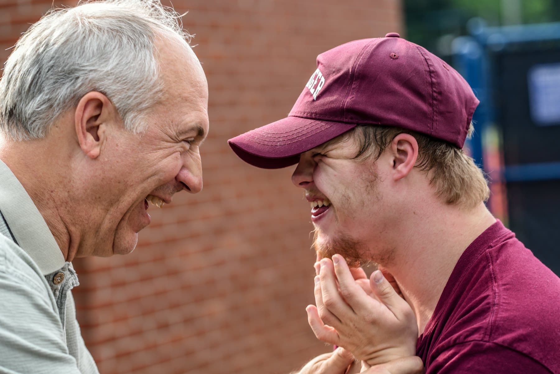 An older man and a young man sharing a joyful laugh outdoors
